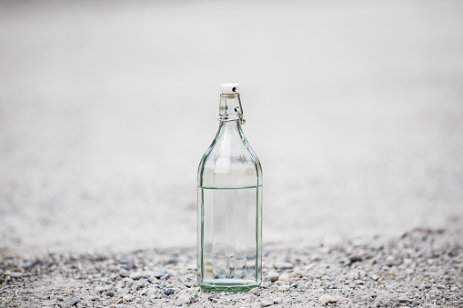 Glass Bottle With Transparent Drink on Gravel.