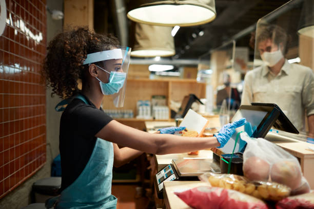 istock A grocery's cashier checking out products wearing protective workwear. 1246278910