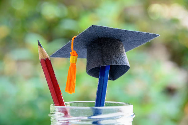 Black graduation cap or a mortarboard, blue and red pencils in a bottle Global education success / graduate study abroad program concept : Image depicting achievement in higher mba learning course in an academy masters degree photos stock pictures, royalty-free photos & images