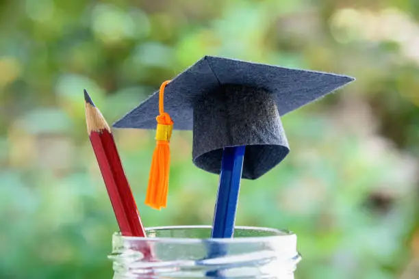 Photo of Black graduation cap or a mortarboard, blue and red pencils in a bottle