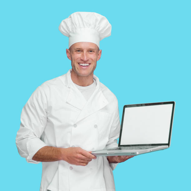 istock Caucasian young male chef standing in front of blue background wearing jacket and using computer 1246294509