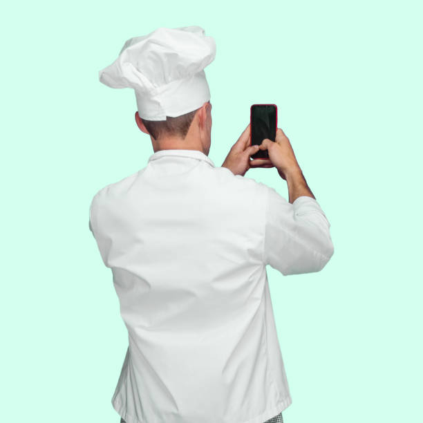 Caucasian young male chef standing in front of colored background wearing pants and using text messaging