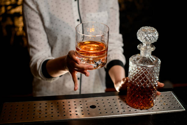 vaso a la antigua con bebida alcohólica en la mano del barman - gin decanter whisky bottle fotografías e imágenes de stock