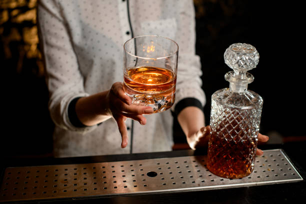 vecchio stile bicchiere con bevanda alcolica in mano barista - gin decanter whisky bottle foto e immagini stock