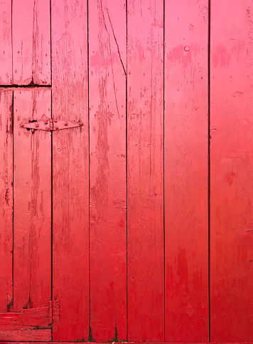 Detail view of a rustic red barn exterior, showing a detail of a freshly painted door and wall coated with red paint. A building exterior background texture featuring barn door hinge details.