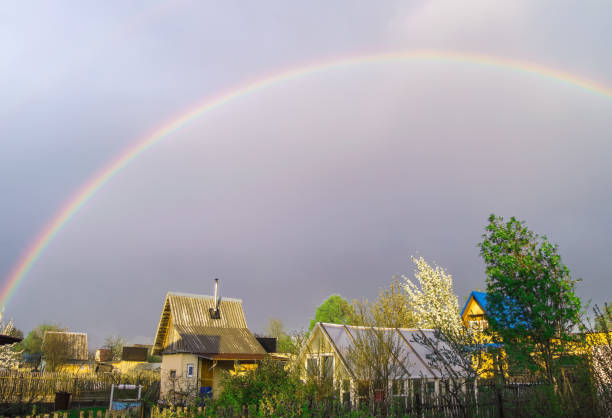 Rainbow over the roofs of rural houses in the stormy evening sky after a storm, summer village landscape stock photo