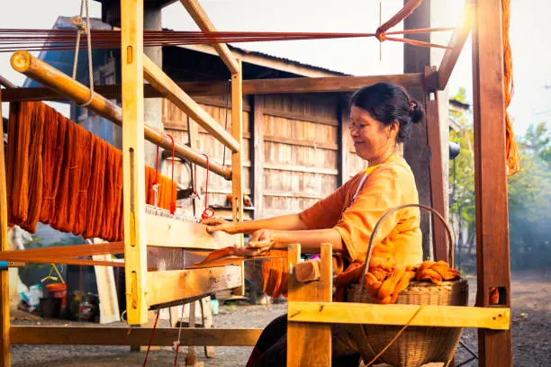 Traditional Isan Thai silk weaving. old woman hand weaving silk Akkanee in traditional way at manual loom. Phu fabric dyeing volcanic igneous or soil. Buriram, Thailand.