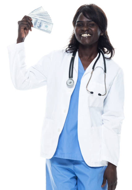 etnia africana giovani donne medico in piedi di fronte a sfondo bianco indossando camice da laboratorio e tenendoci valuta - laughing women us paper currency isolated foto e immagini stock