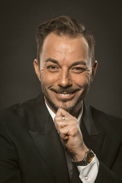 istock Attractive businessman charmingly smiling while looking at the camera and touching his beard with his hand. Close up portrait of mid aged caucasian man. Toned image 1246341178