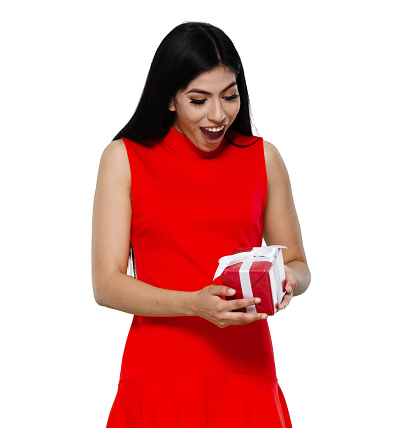 Waist up of aged 20-29 years old who is beautiful with black hair latin american and hispanic ethnicity young women standing in front of white background wearing dress who is happy and holding gift box