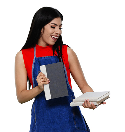 Waist up of aged 20-29 years old who is beautiful with black hair latin american and hispanic ethnicity young women bookseller standing in front of white background wearing apron who is studying and holding book