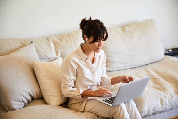 istock Young woman sitting on her sofa working on a laptop 1246363516