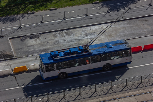 Blue and white urban trolleybus on the streets of a modern city. Top view of the road