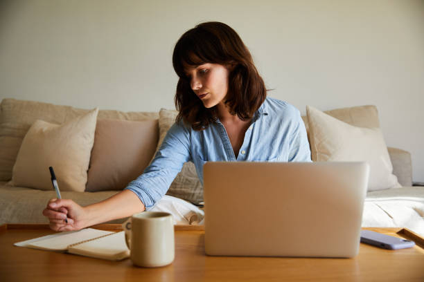 istock Young woman writing notes and working on a laptop at home 1246385892