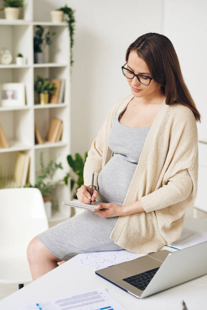 istock Pretty elegant pregnant white collar worker writing down plan for the day 1246387008