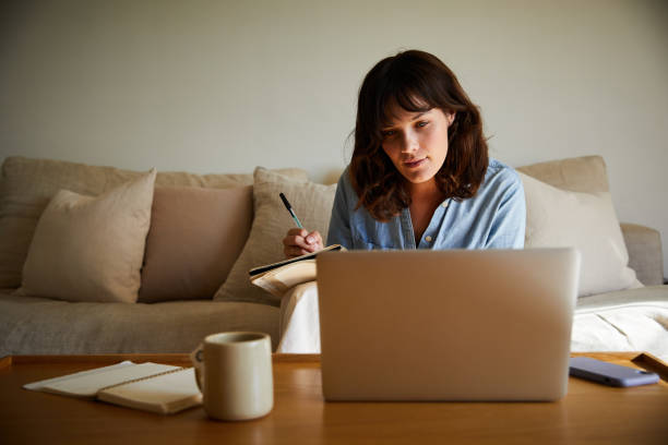 istock Young woman writing notes during a video call at home 1246387022