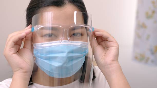 Portrait of an Asia young female who is wearing a face shield with mask rounded around her face from a frontal perspective to protect her glasses and eyes prepare to new normal. Coronavirus pandemic. stock photo