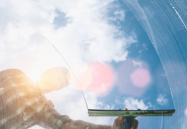 istock Window cleaner cleaning window with squeegee and wiper on a sunny day with a bright blue sky. 1246395918