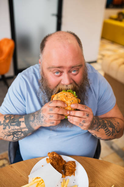 istock Bald man sitting at the table and eating a burger 1246395963