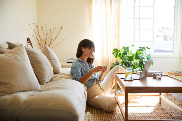 Woman streaming something on a laptop in her living room Young woman sitting on her living room floor at home wearing wireless earbuds and streaming something on a laptop part of a series photos stock pictures, royalty-free photos & images