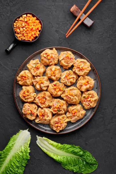 Shumai or Kanom Jeeb or Steamed Pork and Shrimp Dumplings on a black plate on dark slate backdrop. Shumai is a chinese cuisine dish with minced pork meat, shrimps, and vegetables. Chinese food