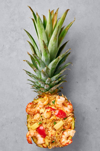 Thai Pineapple Fried Rice or Kao Pad Sapparod dish in pineapple bowl on gray backdrop. Thailand meal. Asian Food.