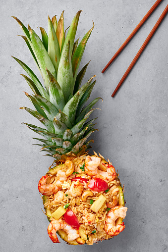 Thai Pineapple Fried Rice or Kao Pad Sapparod in cutted pineapple bowl on gray concrete background. Kao Pad Sapparod is a Thai Cuisine dish with rice, shrimps, pineapple, tomatoes and cashew nuts