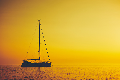 Silhouette of a sailing boat in sunset / sunrise time and ocean horizon.