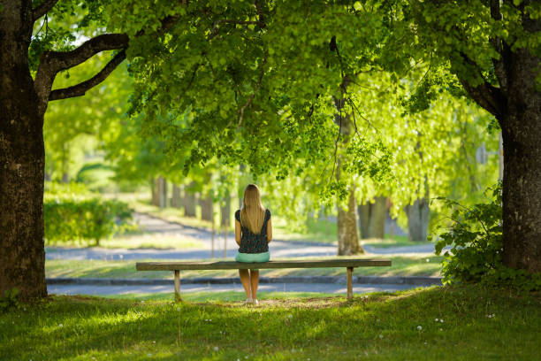 istock One young woman sitting alone on bench between trees at beautiful green park. Thinking about life. Spending time alone in nature. Peaceful atmosphere. Back view. 1246468529