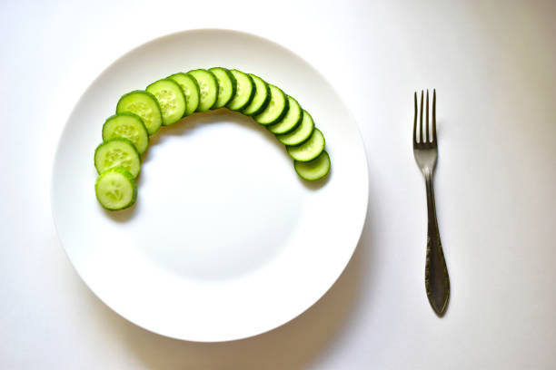 Sliced green cucumber on a white plate and a fork
