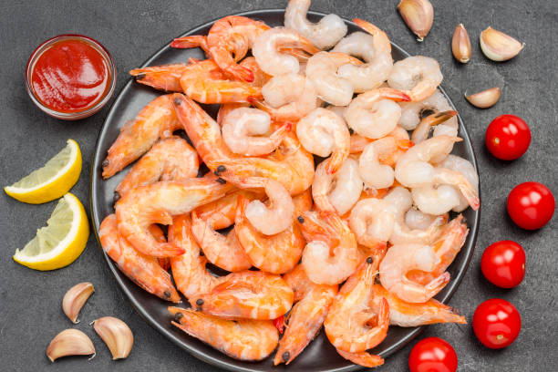 istock Tiger prawns and shrimp in black bowl. Tomatoes, garlic cloves lemon on table. 1246475845