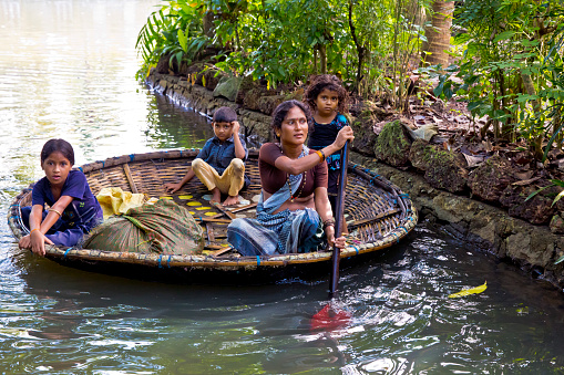 Kumarakom, Kerala/India - September 23, 2013: On an early morning - a woman with her three young kids, on a bamboo raft, going about their daily activities in the backwaters of Kerala.