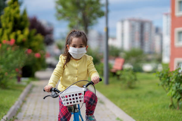 istock Little girl in protective face mask rides bicycle 1246501208
