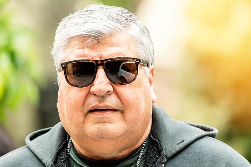 Overweight mature senior hispanic man posing looking ay the camera wearing sunglasses