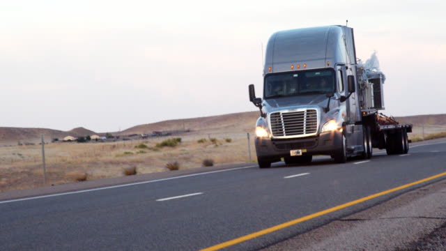 A Long Haul Semi-Truck and Trailer Heading Down a Four-Lane Highway in the Desert at Dawn or Dusk