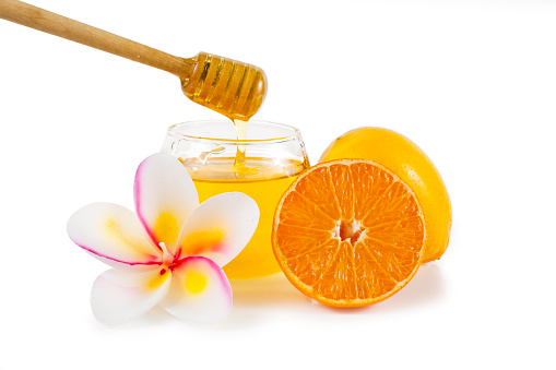 Honey with lemon, candles in the shape of frangipani flowers and orange fruits isolated on a white background.