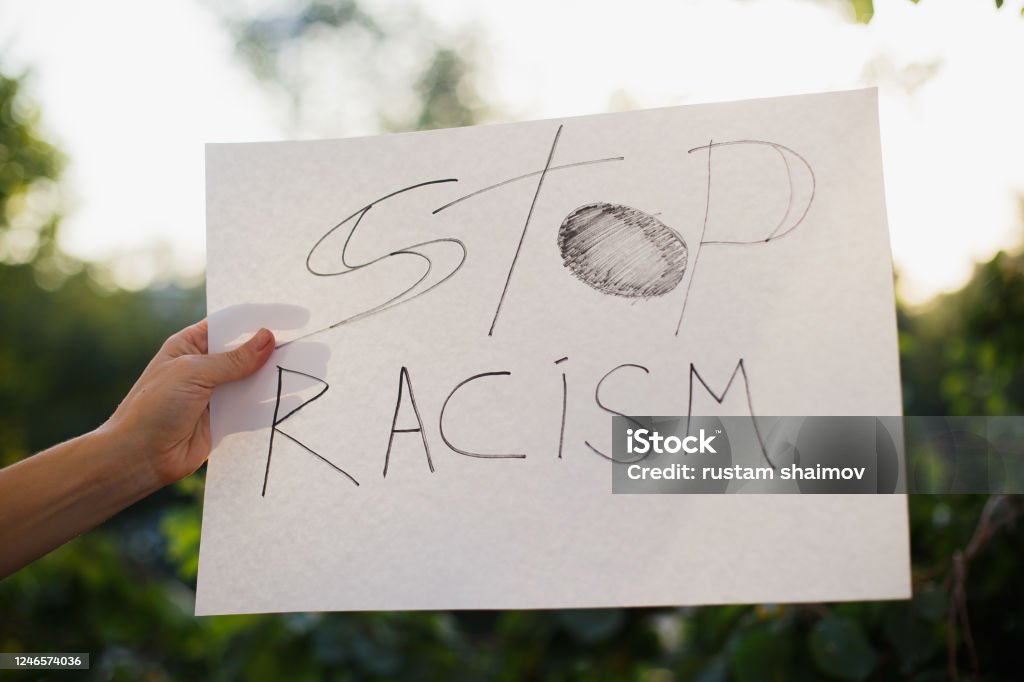 Woman holding white paper with text "Stop racism". Woman holding white paper with text "Stop racism". Against the background of trees and sunlight Anti-racism Stock Photo