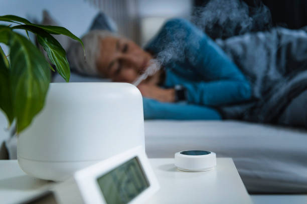 Air Humidifier Increasing the Humidity in a Bedroom. Beautiful Mature Woman Sleeping in Bed. Air Humidifier increasing the humidity in a bedroom for better sleep. Beautiful mature woman sleeping in bed. air quality stock pictures, royalty-free photos & images