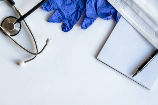 istock Workplace of doctor with notebook, gloves, mask and stethoscope on keyboard and notepad with pen on light blue backround. Copy space. Close up. Top view. Concept medical, business. 1246599287