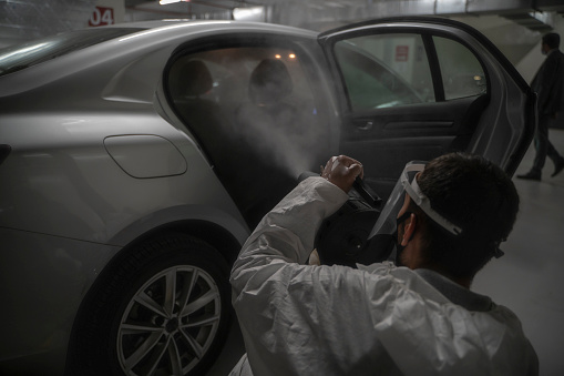 Covid-19 virüsü ile mücadele kapsamında araçların dezenfekte çalışmalarını yapan adam, otomobilleri ilaçlıyor.