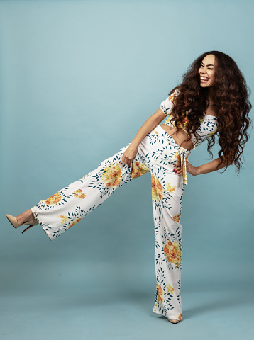 Beautiful woman with long curly hair in floral outfit front of blue background
