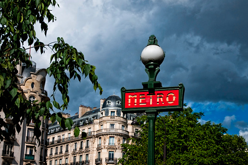 A Metro transportation sign in paris, France, with an old apartment building in the background - Panneau extérieur du métro parisien.