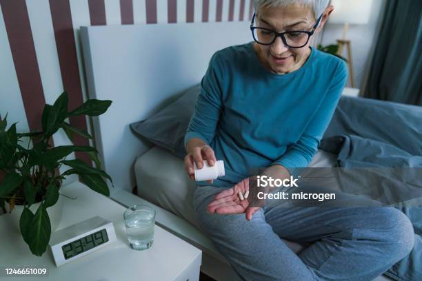Melatonin For Promotion Of Healthy Sleep Mature Woman Taking Melatonin Supplement Pill Before Bed Stock Photo - Download Image Now