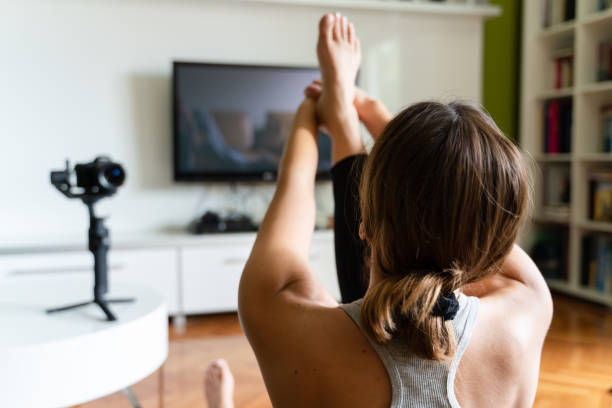 istock Young caucasian woman practicing yoga at home beautiful instructor teaching online class training in the apartment talking in front of camera and laptop making video blog or vlog back view real people daily routine and balance concept 1246682512