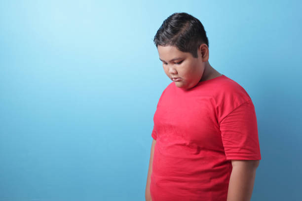 Fat Asian boy, looking down, sad and crying, bullied concept with copy space Fat Asian boy looking down, sad and crying, being bullied, sadness, child abuse concept, against blue background overweight child stock pictures, royalty-free photos & images