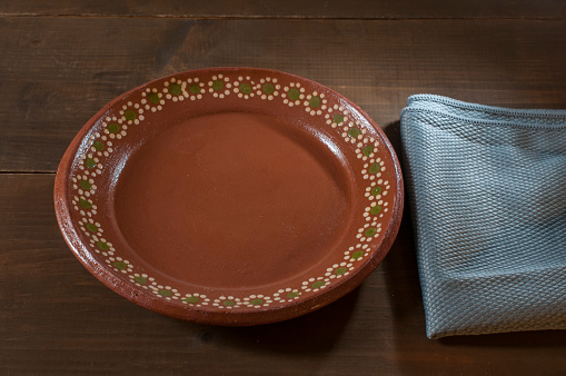 Mexican plate made of clay or mud on a rustic wooden table and a blue napkin. Culture of Mexico. Still life photography