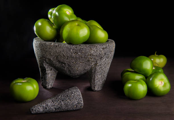 TOMATILLOS and MOLCAJETE Mexican kitchen concepts A bunch of Tomatillos or husk tomato in a molcajete in dark food photography in a black background on a wooden rustic table. Concept of Mexican food ingredients to make spicy salsa verde. Still life tomatillo photos stock pictures, royalty-free photos & images