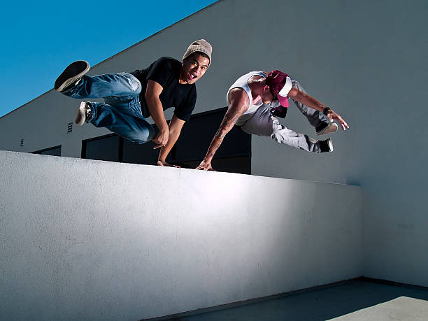 zwei männliche freerunner springt über die mauer performing parkour - le parkour stock-fotos und bilder