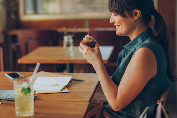 istock Young Woman Eating a Delicious Cupcake While Working at a Cafe 1246728458