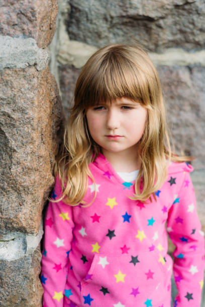 istock A sad little girl is standing beside a brick wall. 1246751526